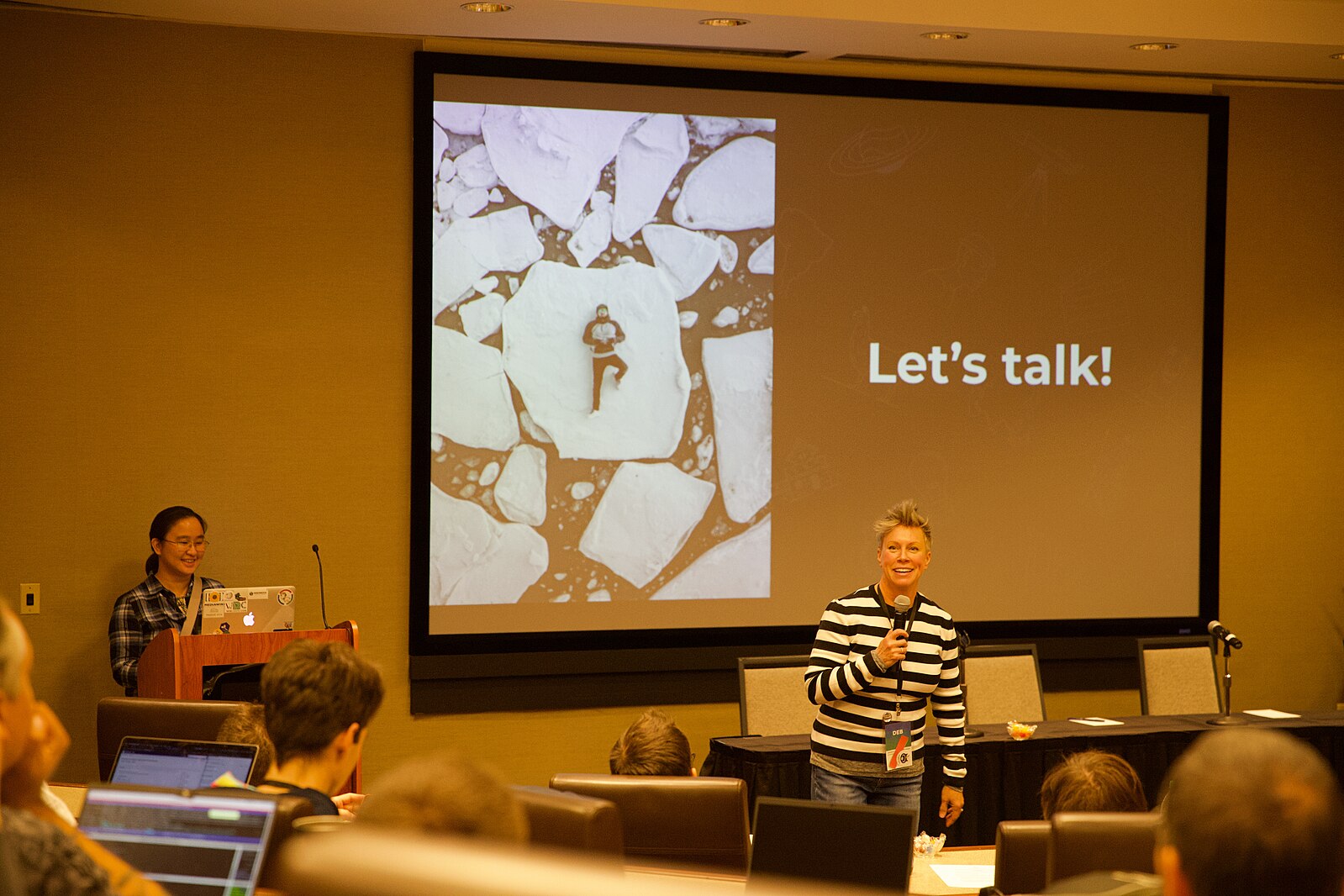 Person stood with micrphone in front of screen showing words “let’s talk”